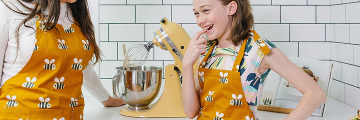 Apron with bees hands in oven mitts holding a pavlova